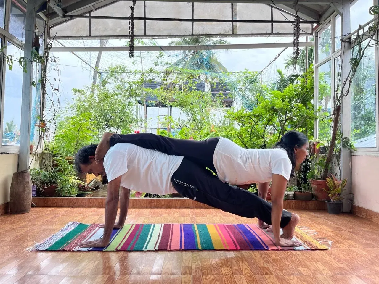 Stacked partner plank on a yoga mat in the plant-filled studio, 50-hour yoga teacher training
