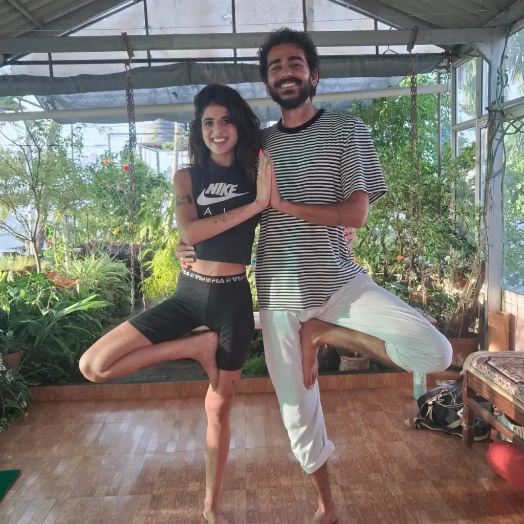 Two guests smiling in partner tree pose in the garden shala