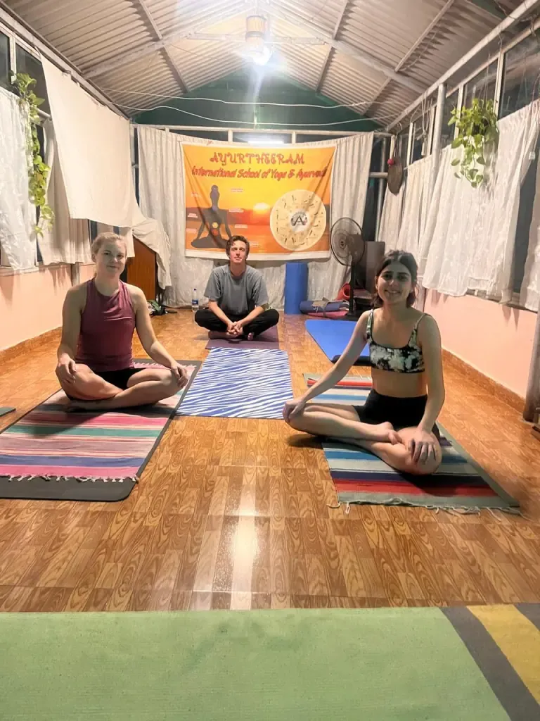 Three guests seated cross-legged on mats in an evening yoga class