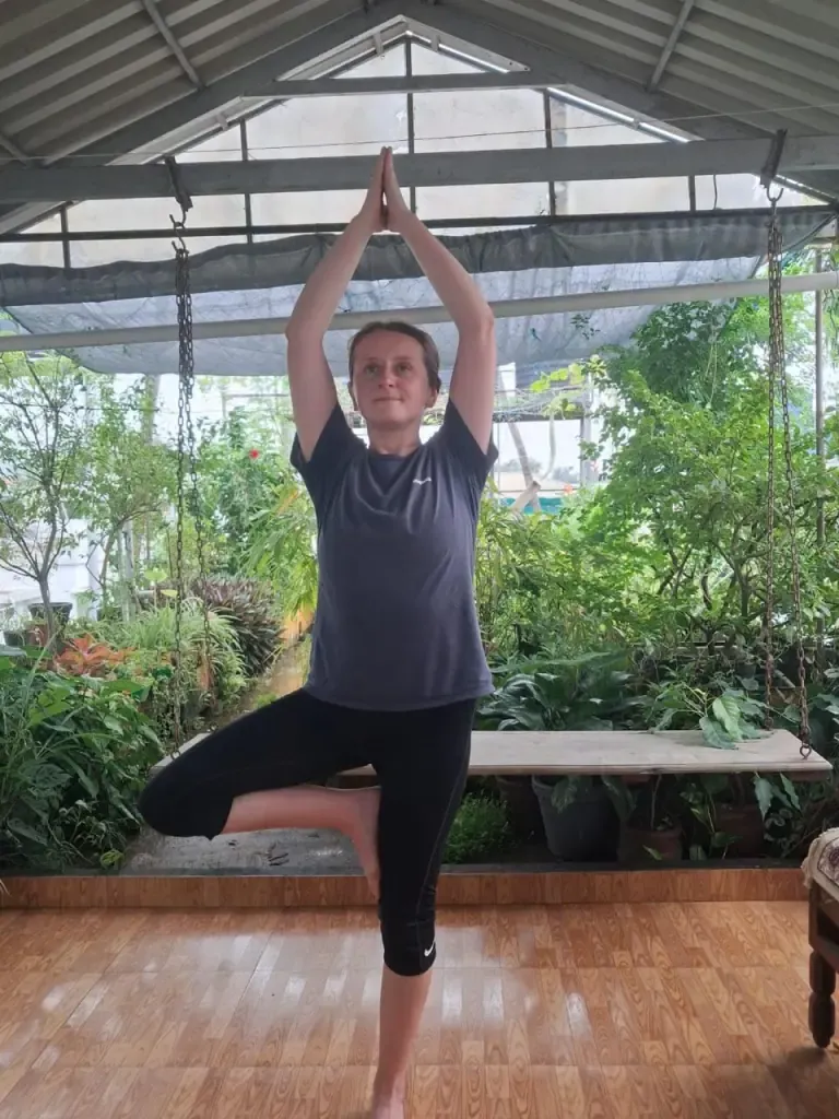 A guest in tree pose with arms raised overhead in the rooftop garden shala