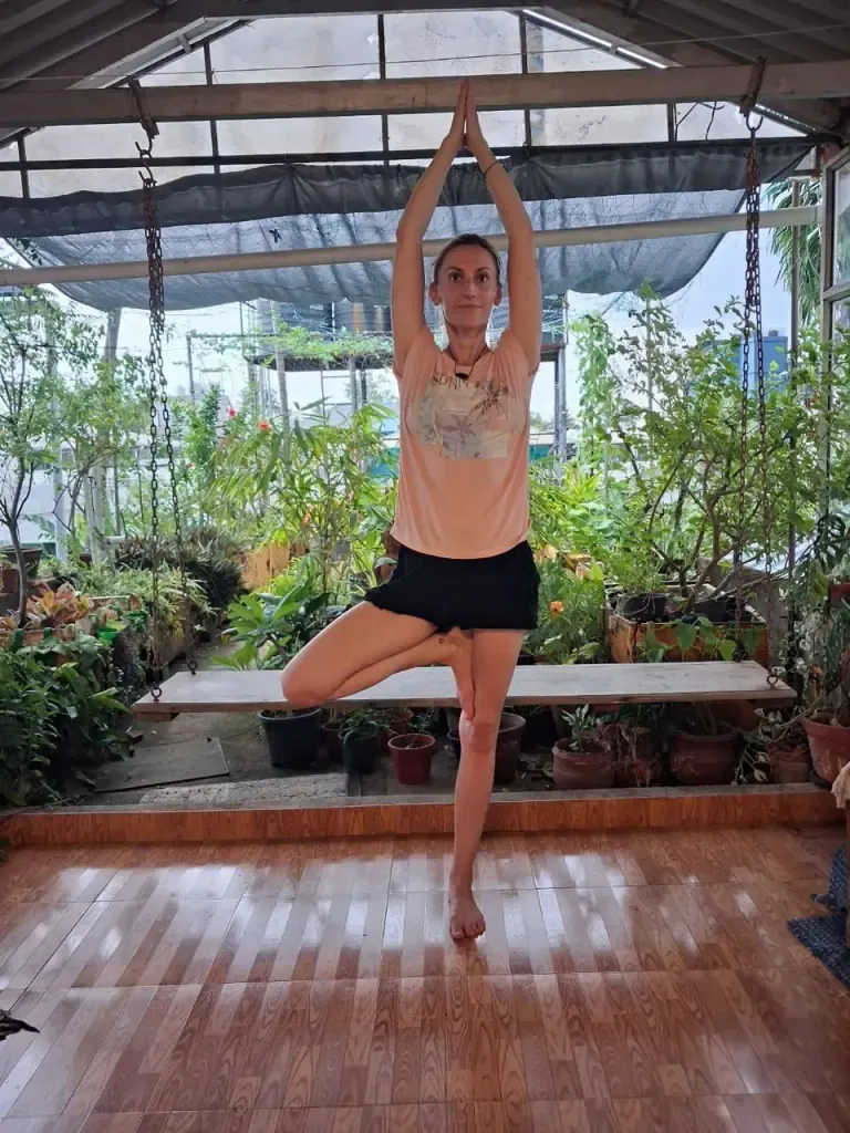 A guest in tree pose with arms raised in front of the garden swing