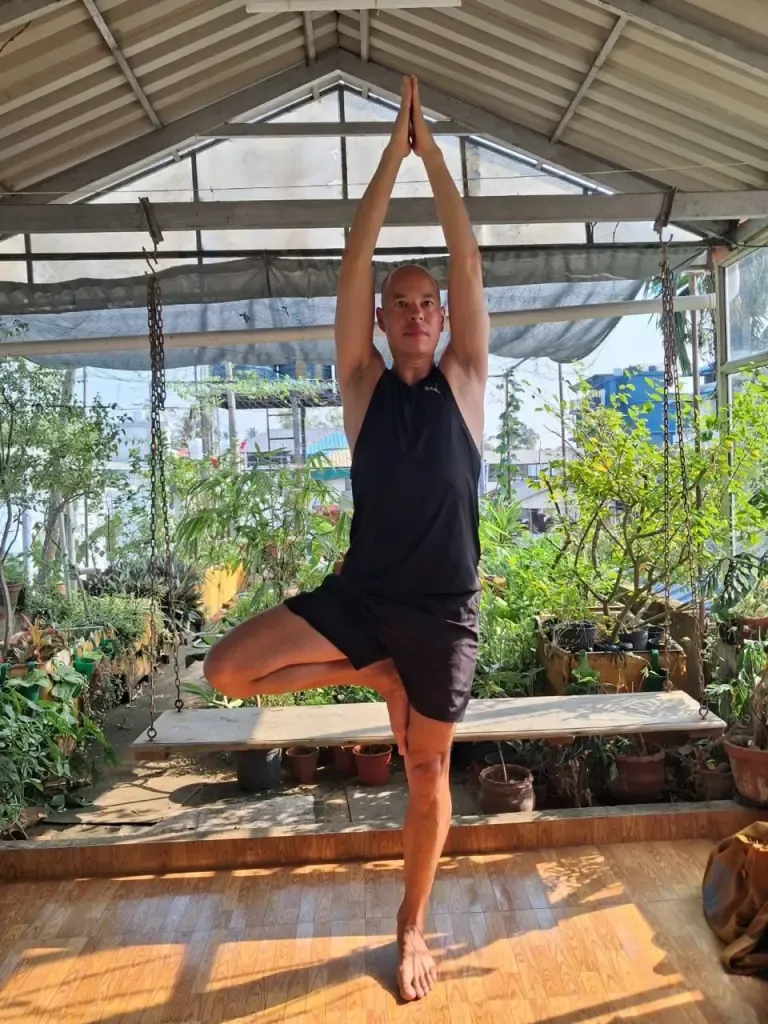 A guest in tree pose with arms stretched overhead in the sunlit shala