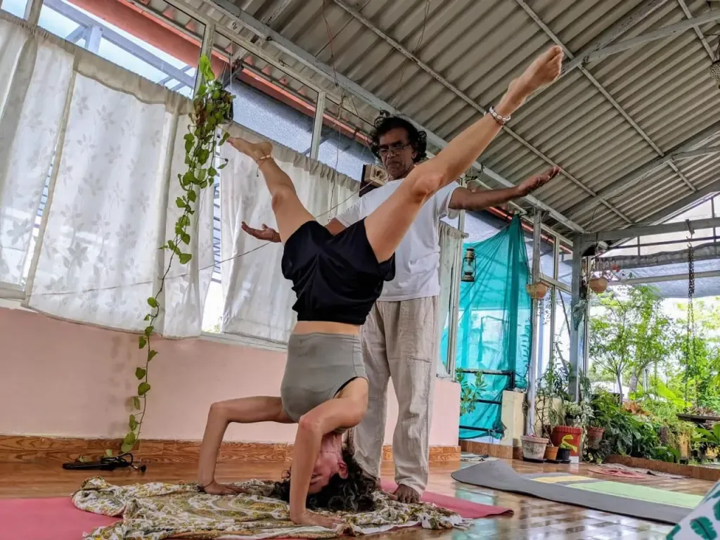 A guest in a headstand with legs split while the teacher guides the pose
