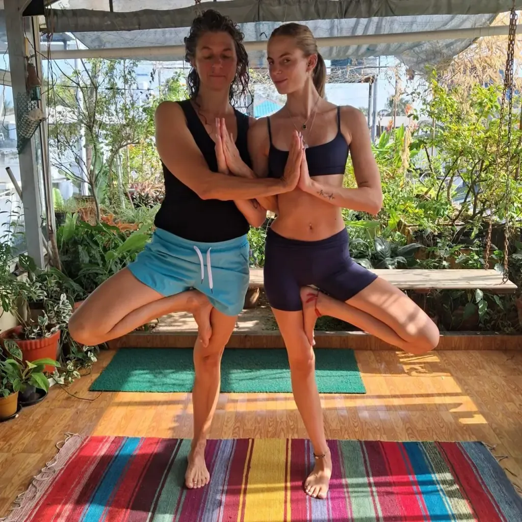 Two guests in partner tree pose on a striped rug in the rooftop garden