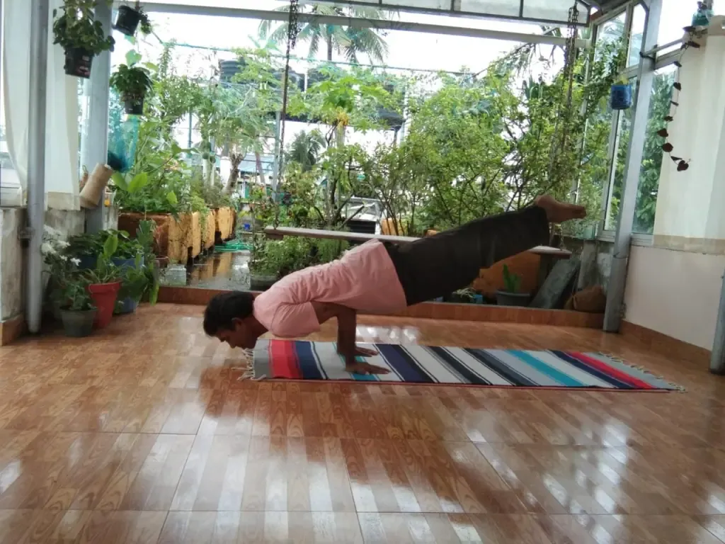 An arm balance in peacock pose on a striped mat in the rooftop shala