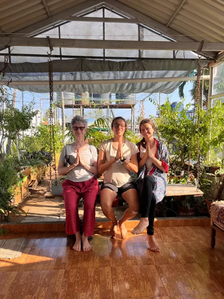 Three guests seated on the garden swing with hands in namaste