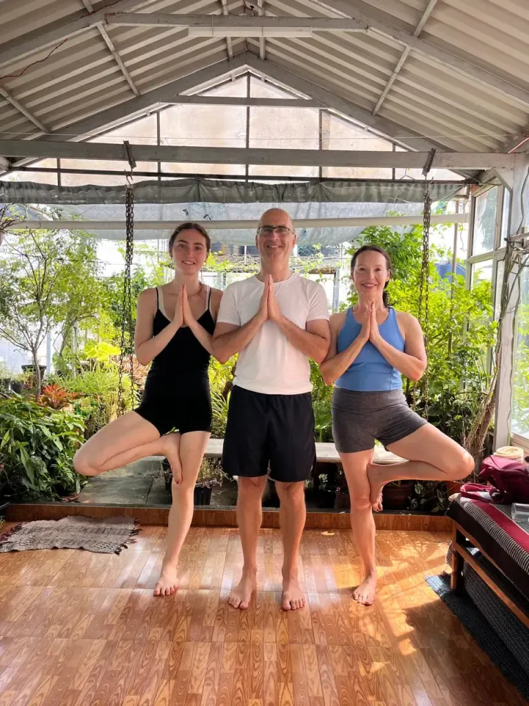 Three guests in tree pose with hands in namaste in the garden shala